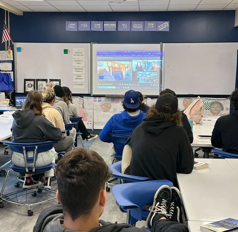 a group of students sit in a classroom attending a Zoom session with a Pulitzer Center journalist