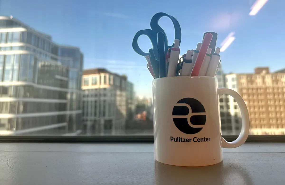 Pulitzer Center mug with pens and scissors in front of window with city view